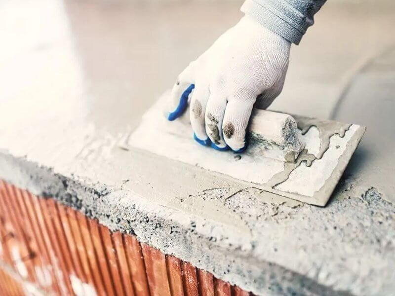 Gloved hand spreading wet concrete over a brick surface with a trowel