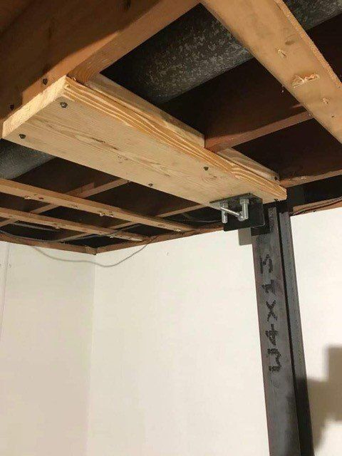Underside of a wooden loft bed frame with a black metal support post in a room corner