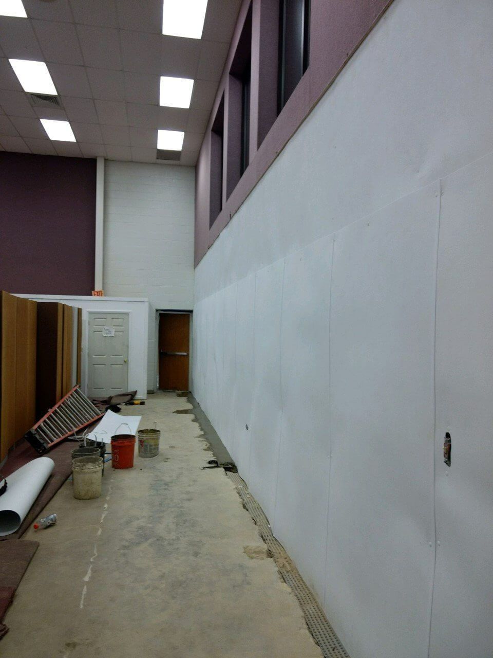 Long narrow hallway with construction materials, a white wall, and overhead fluorescent lights