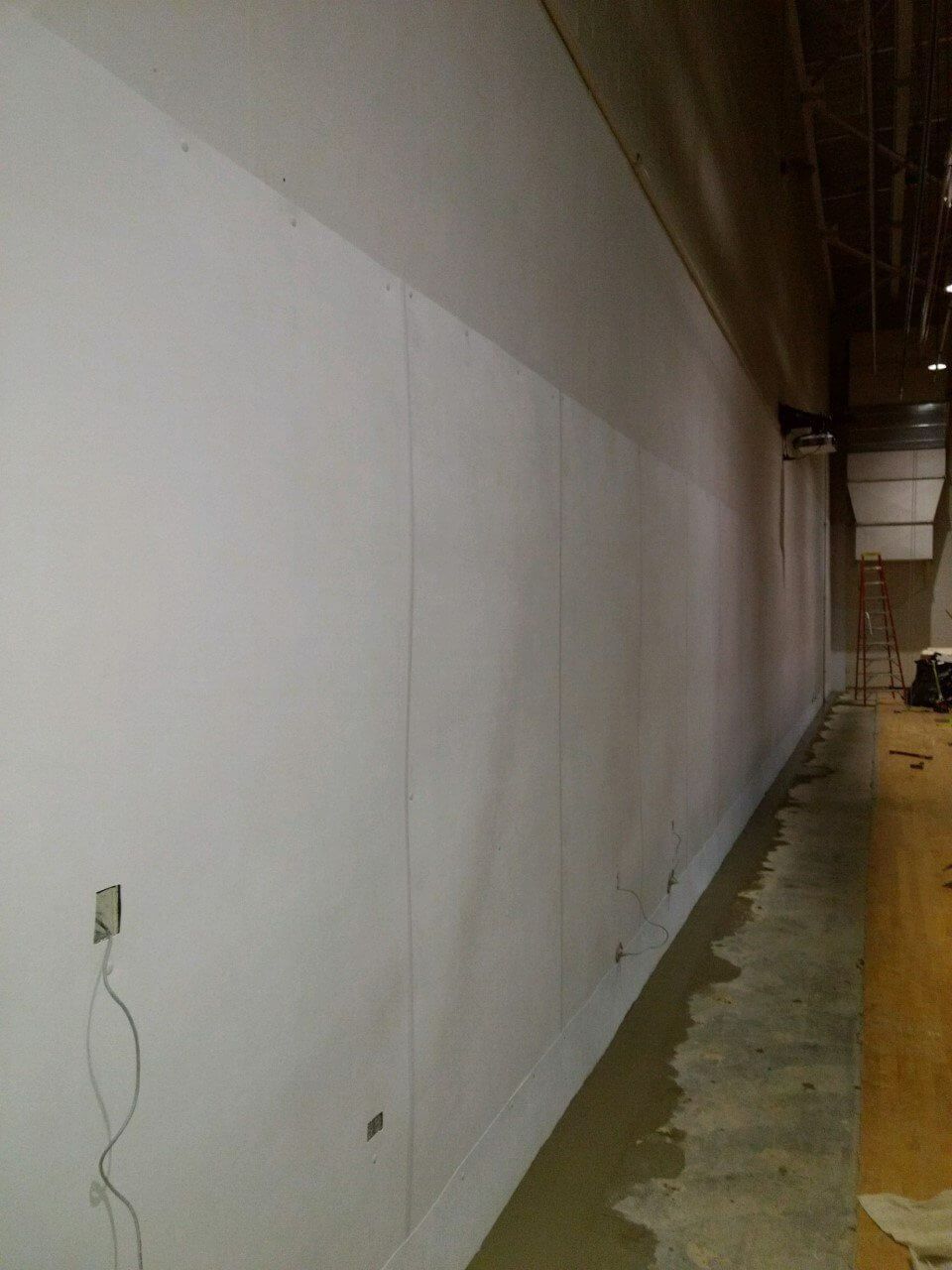 Long white wall in a narrow industrial hallway with a yellow floor and ceiling lights