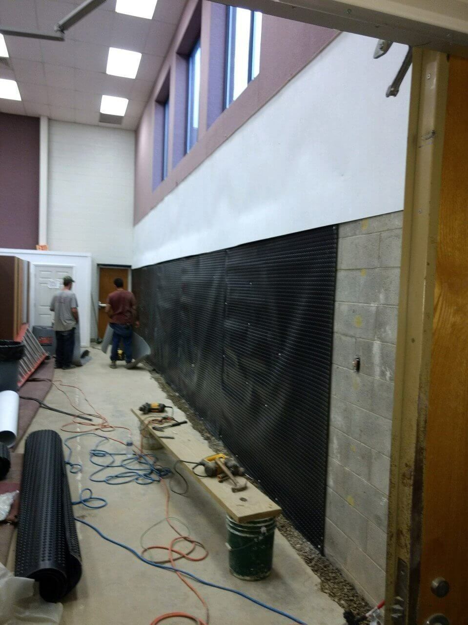 Long hallway under renovation with black wall covering, tools, cables, and two workers near the far end