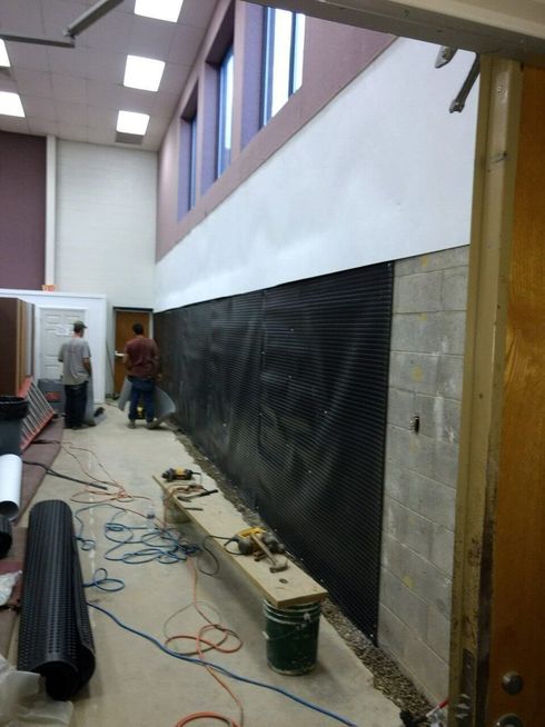 Long hallway under renovation with black wall covering, tools, cables, and two workers near the far end