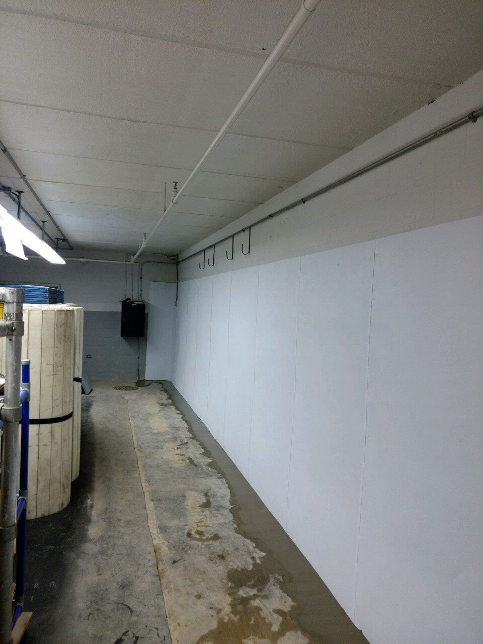 Narrow industrial hallway with white walls, exposed ceiling, and large metal tanks along the left side.