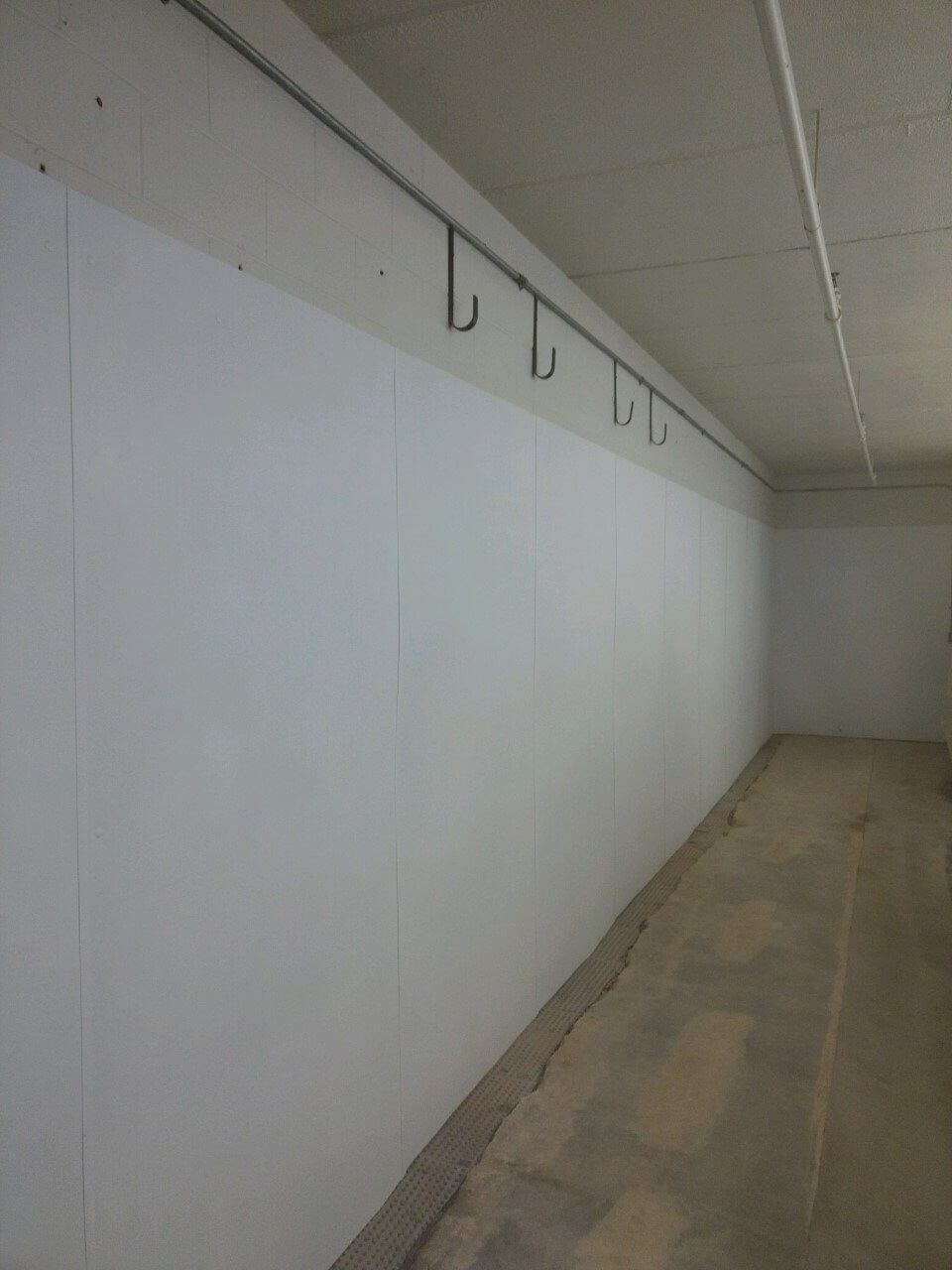 Empty white hallway with hooks along the wall and a beige floor.