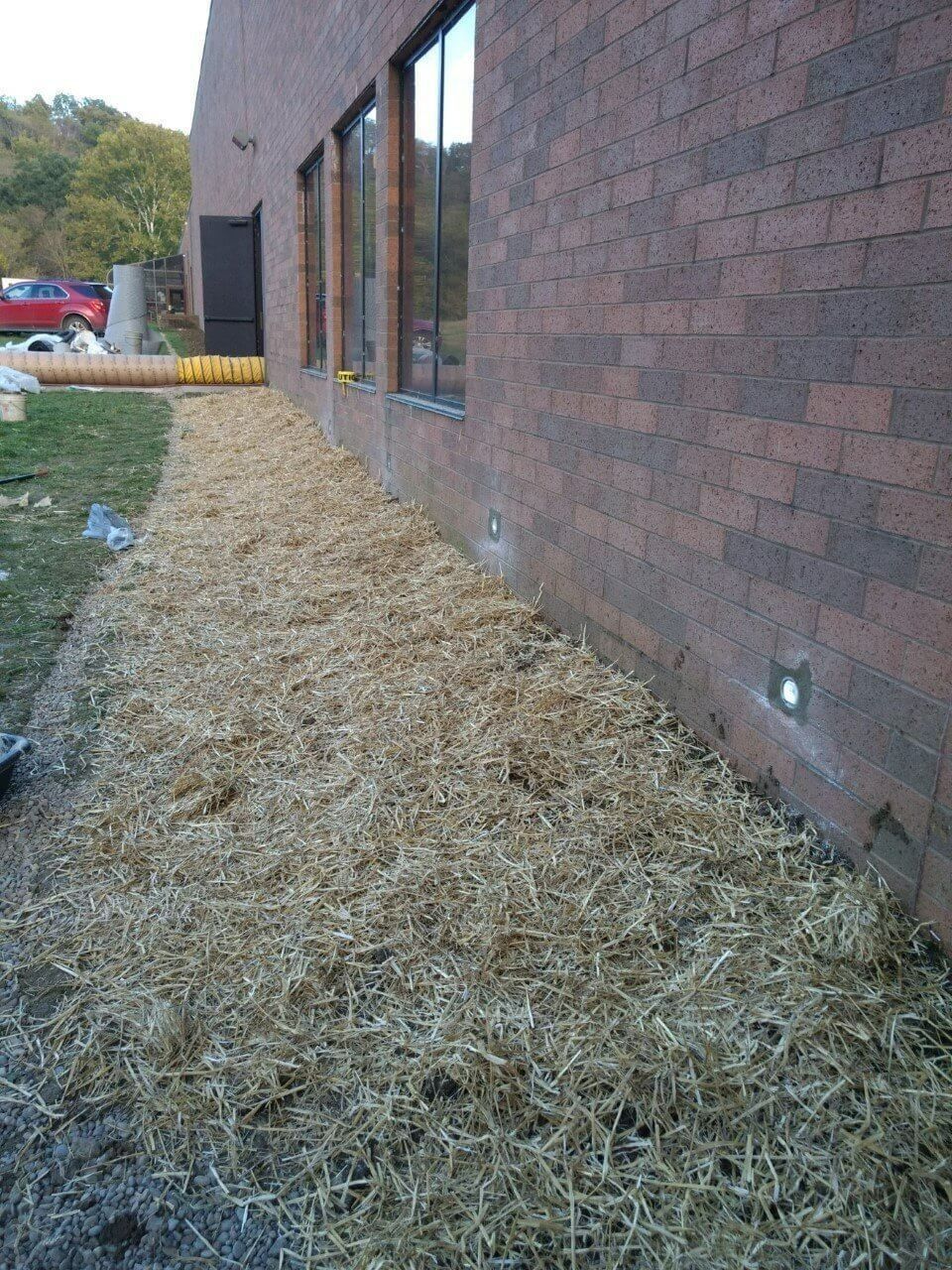 Mulch piled along a brick building exterior with windows and small ground lights