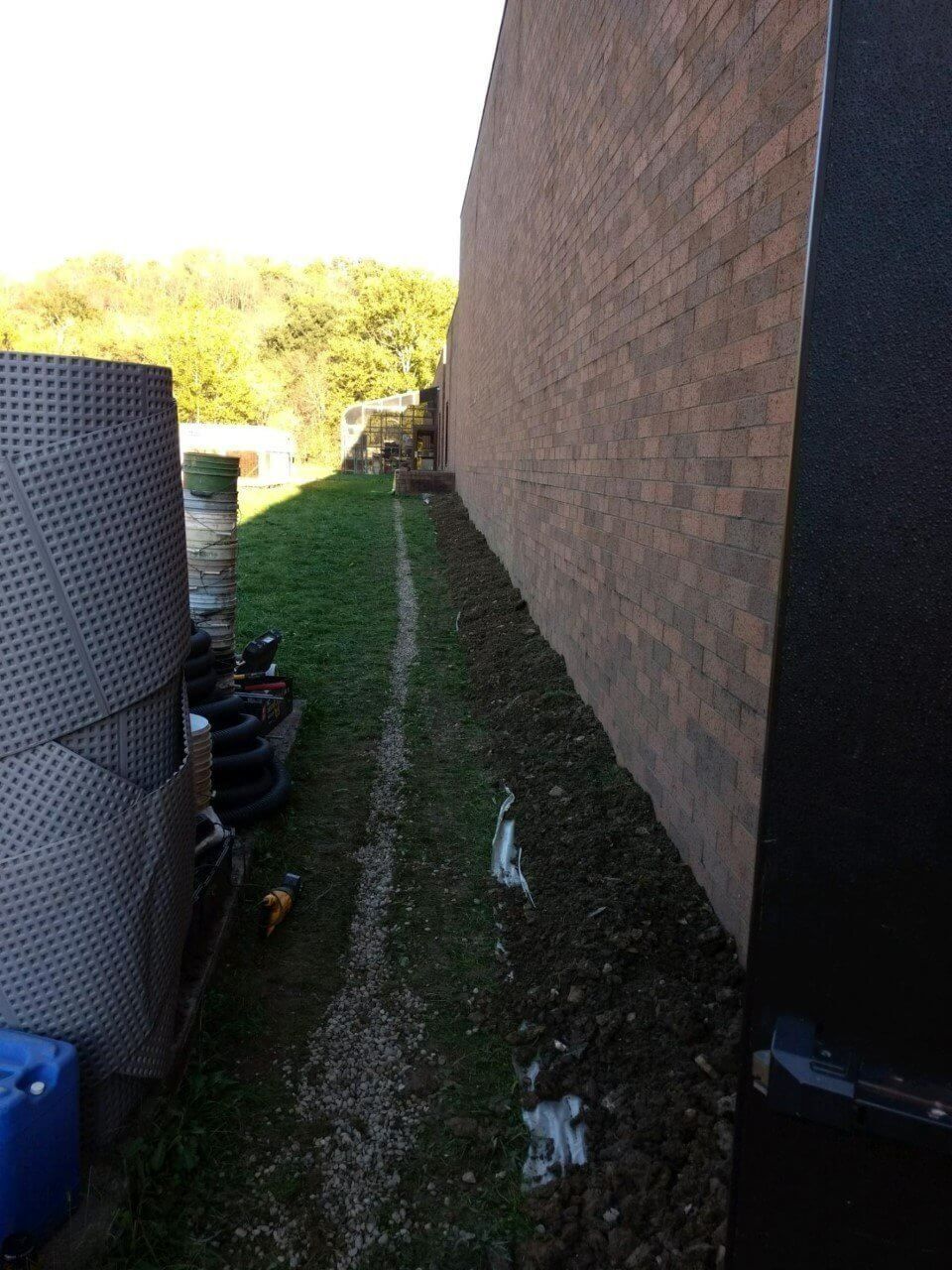 Narrow grassy side yard beside a brick wall, with outdoor equipment along the left side.