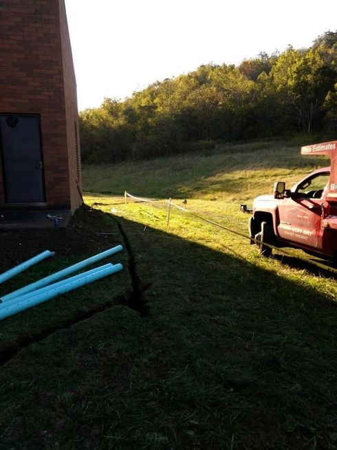 Red pickup truck by a brick building beside a grassy field at sunset