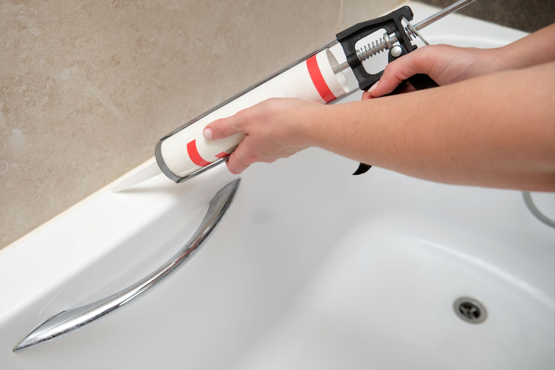 A person is applying caulk to the edge of a bathtub.