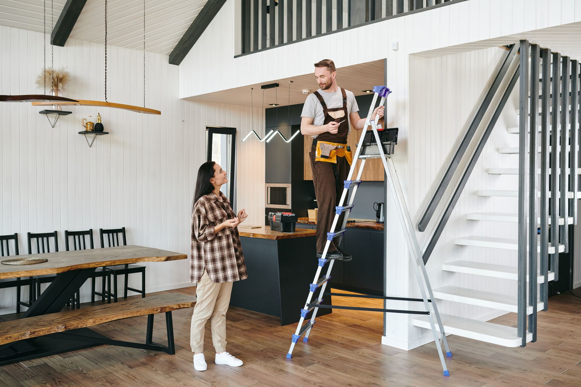 A man is standing on a ladder next to a woman in a living room.