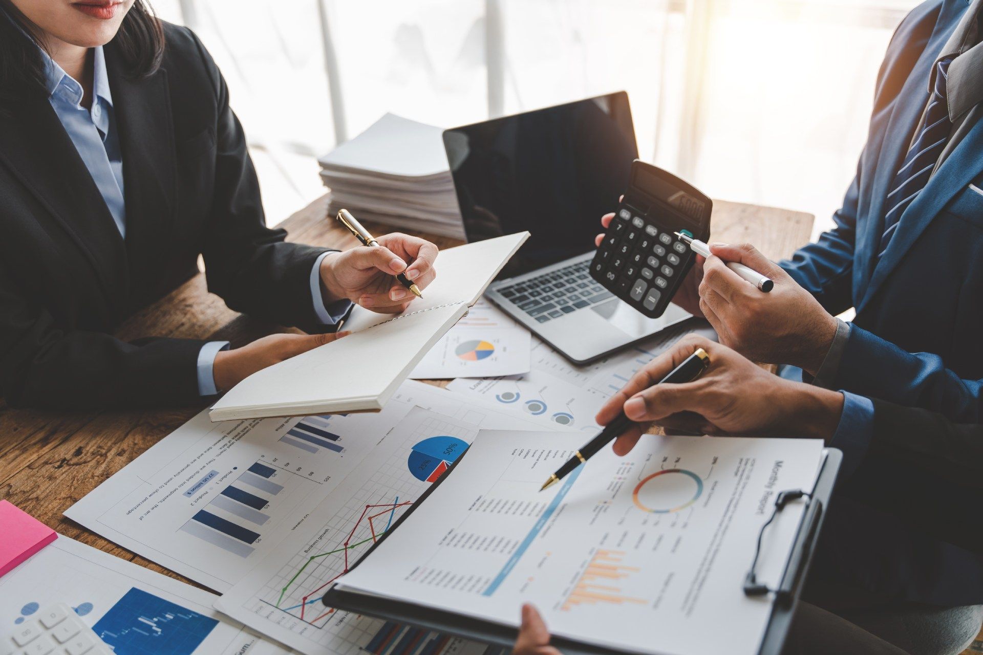 People reviewing financial documents with a laptop, calculator, and pen in an office setting.