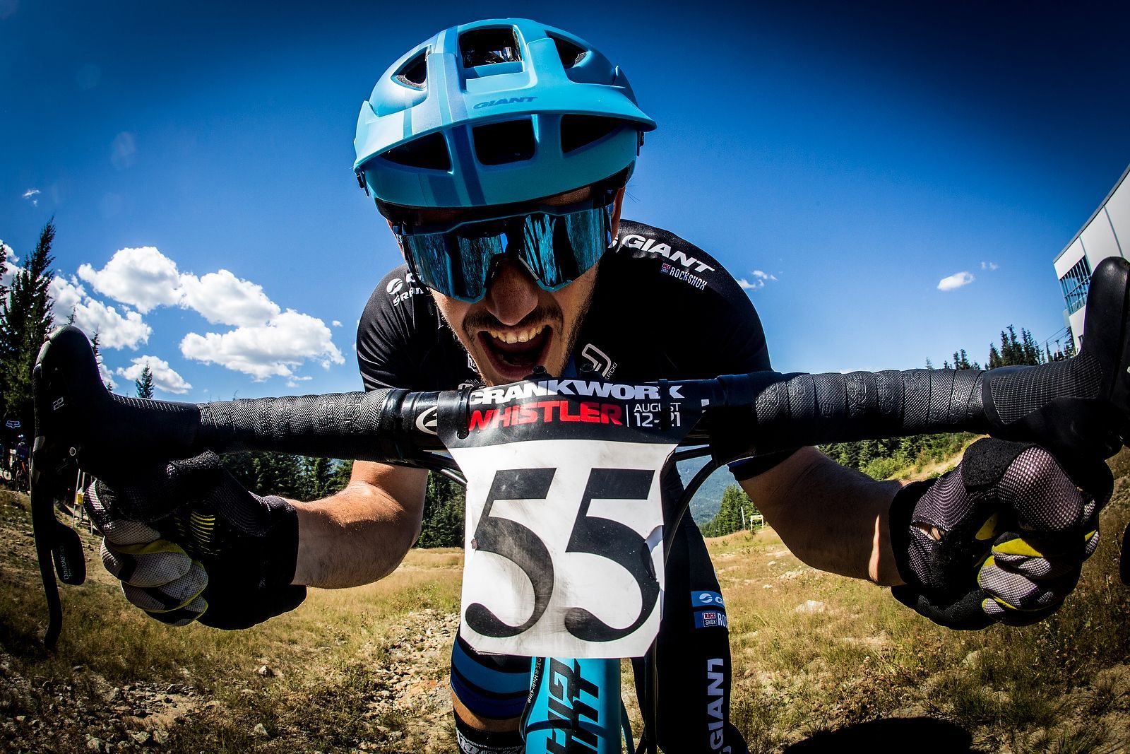 A man wearing a helmet and sunglasses is riding a bike with the number 55 on the handlebars.