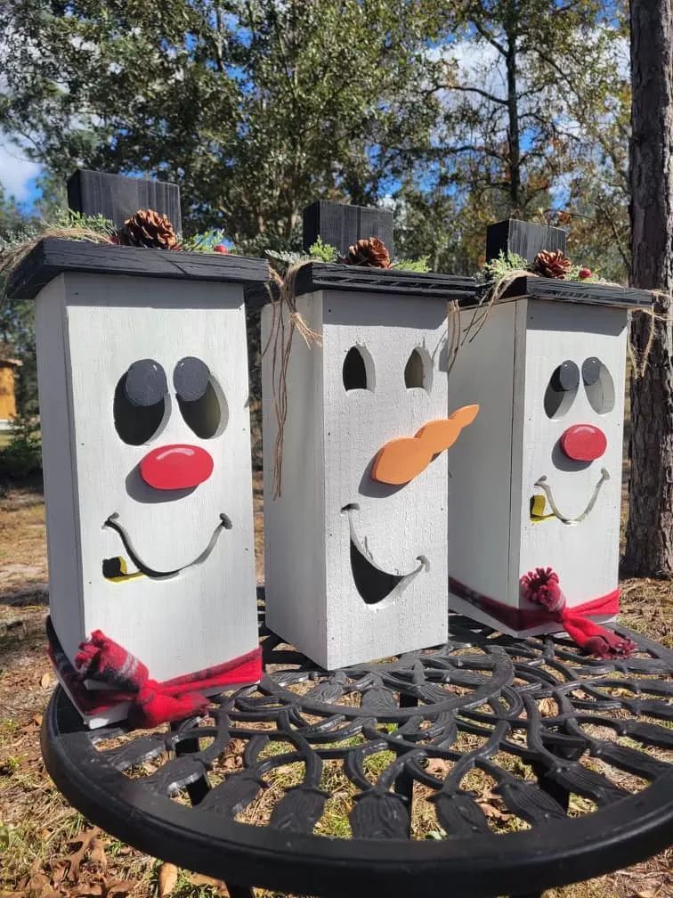 Three snowmen made out of wood are sitting on a table.