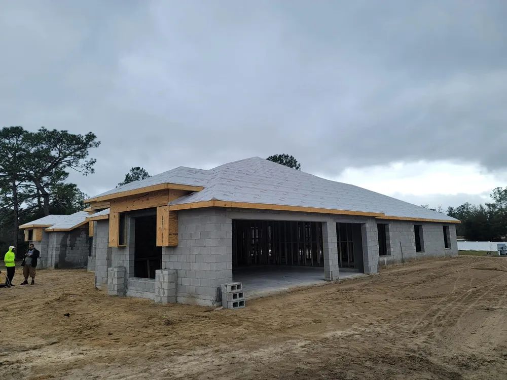 A house is being built in a dirt field with a cloudy sky in the background.