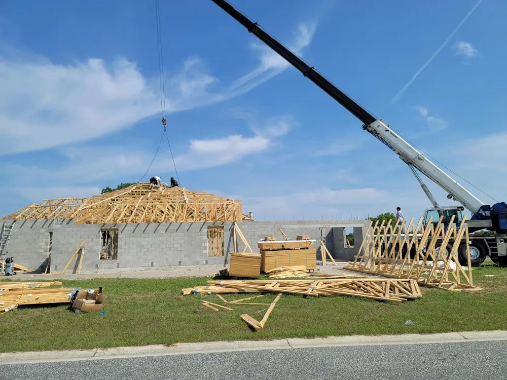 A crane is lifting a piece of wood in front of a house under construction.