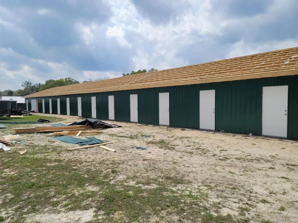 A large green building with white doors is being built in a dirt field.
