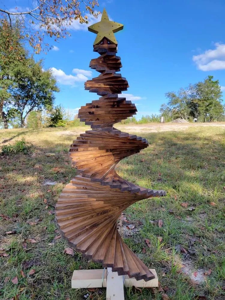A wooden spiral christmas tree with a star on top is sitting in the grass.