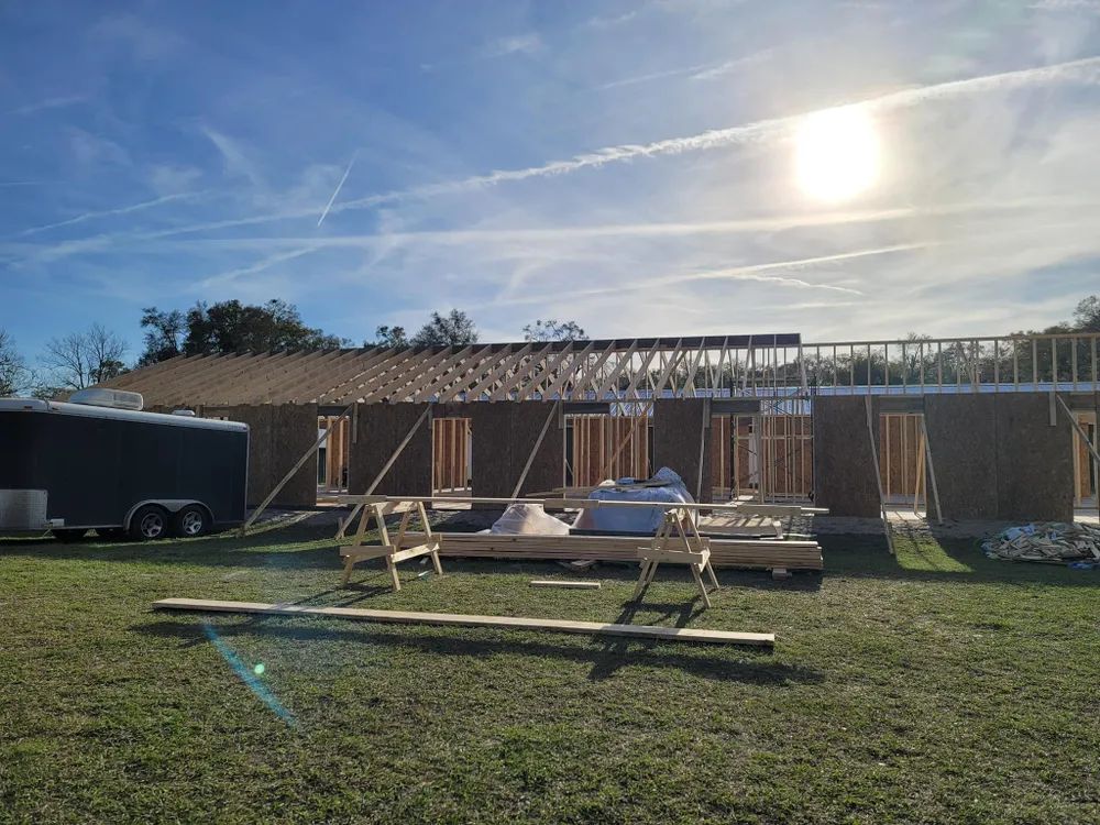 A house is being built in a grassy field with a trailer in the background.
