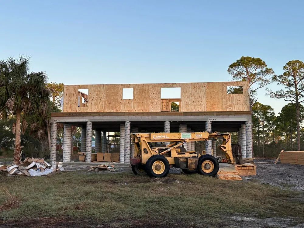 A yellow forklift is parked in front of a house under construction.
