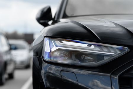 A close up of a black car 's headlight in a parking lot.