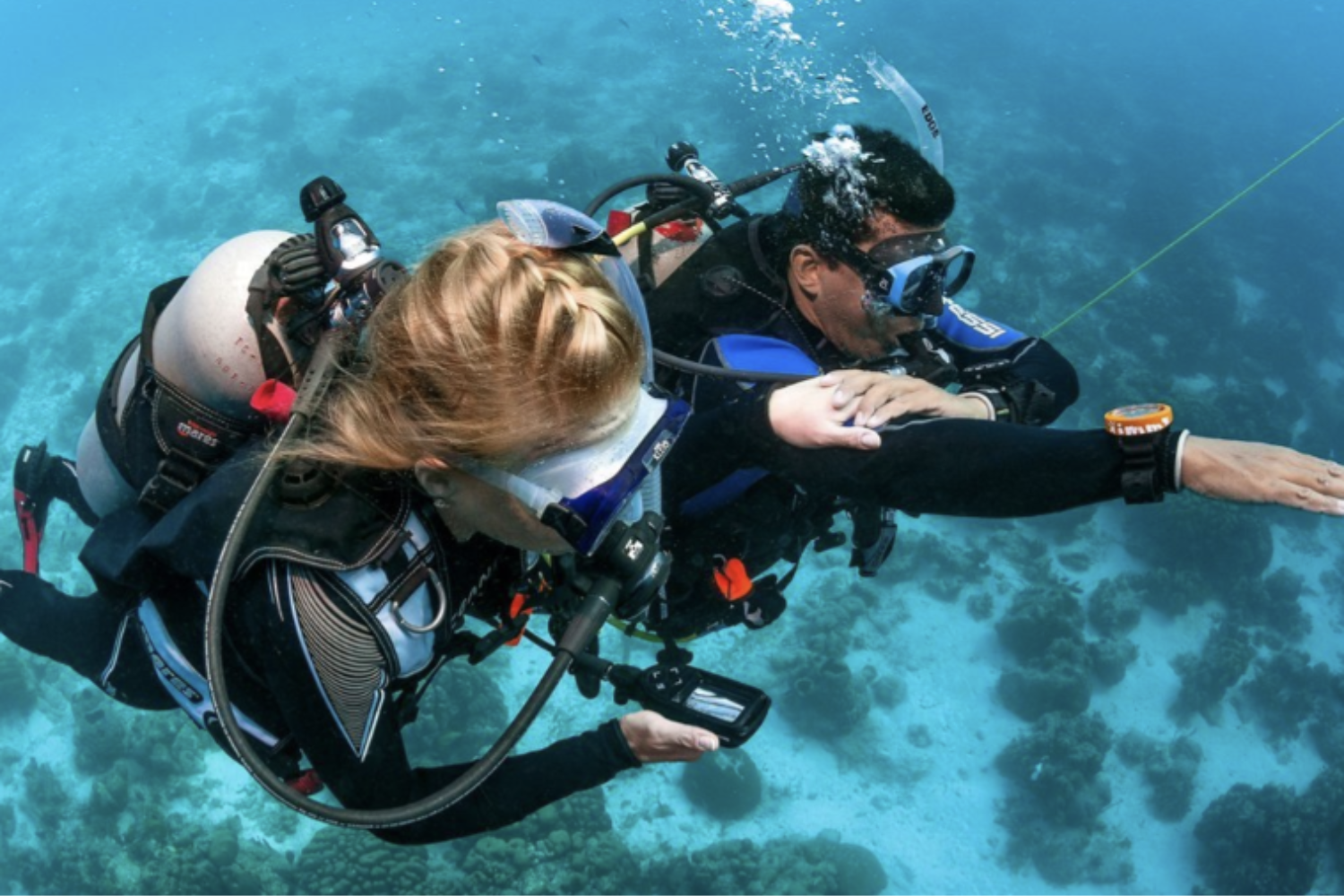 A man is teaching a woman how to scuba dive in the ocean.