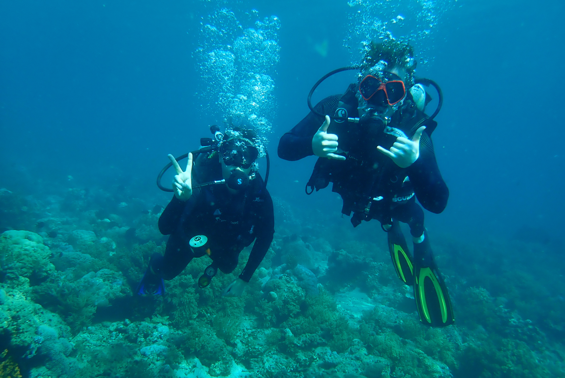 Two scuba divers are giving the thumbs up sign in the ocean.