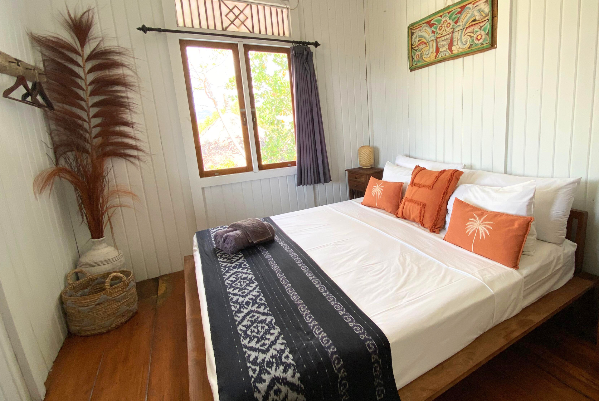Bedroom with white walls, wood bed, orange pillows, and a black and white patterned blanket.