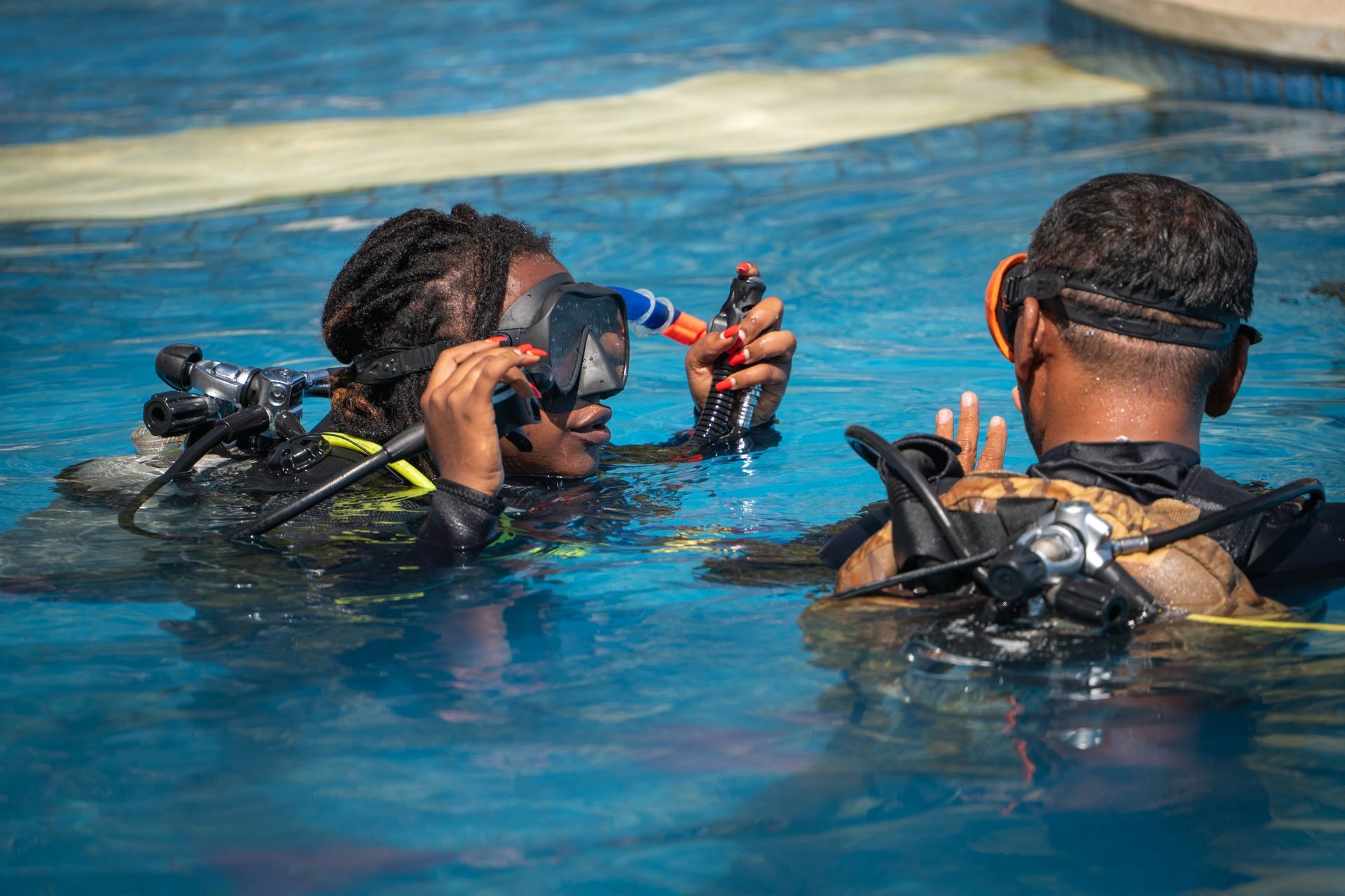 A man is teaching a woman how to scuba dive in a swimming pool.
