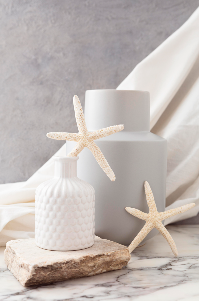 Dos jarrones con estrellas de mar sobre un fondo de piedra y tela blanca.