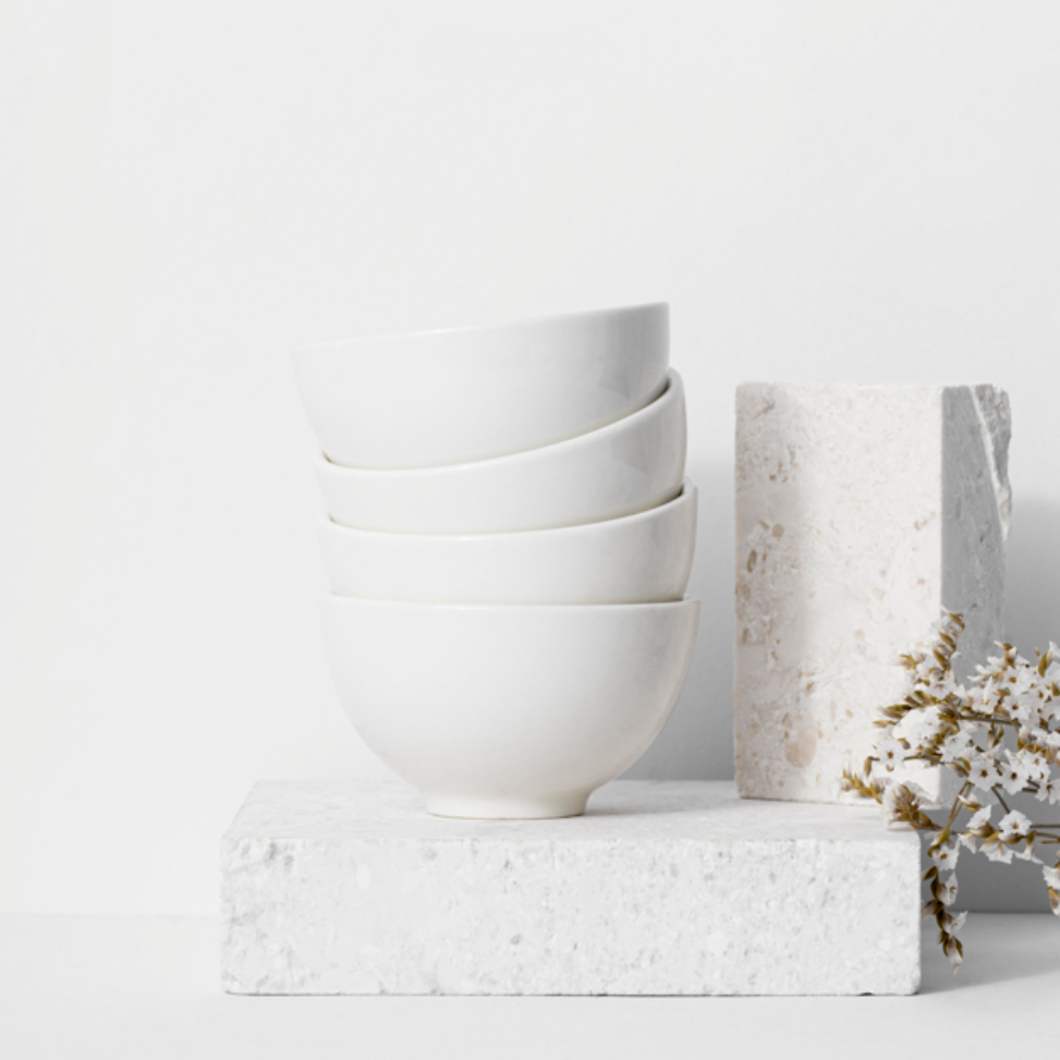 Pila de cuencos blancos sobre un bloque blanco con una piedra decorativa y flores secas.