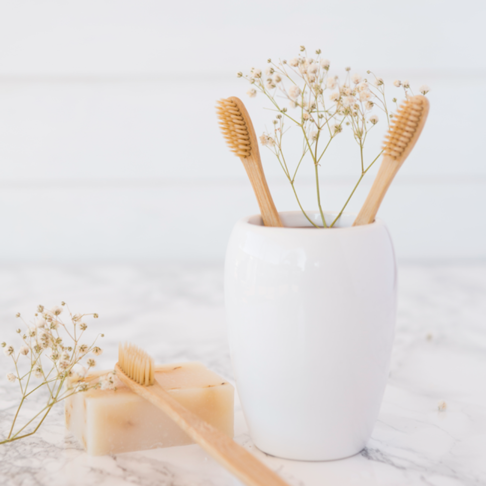 Tres cepillos de dientes de bambú y jabón en una taza blanca, con aliento de bebé, sobre una superficie de mármol.