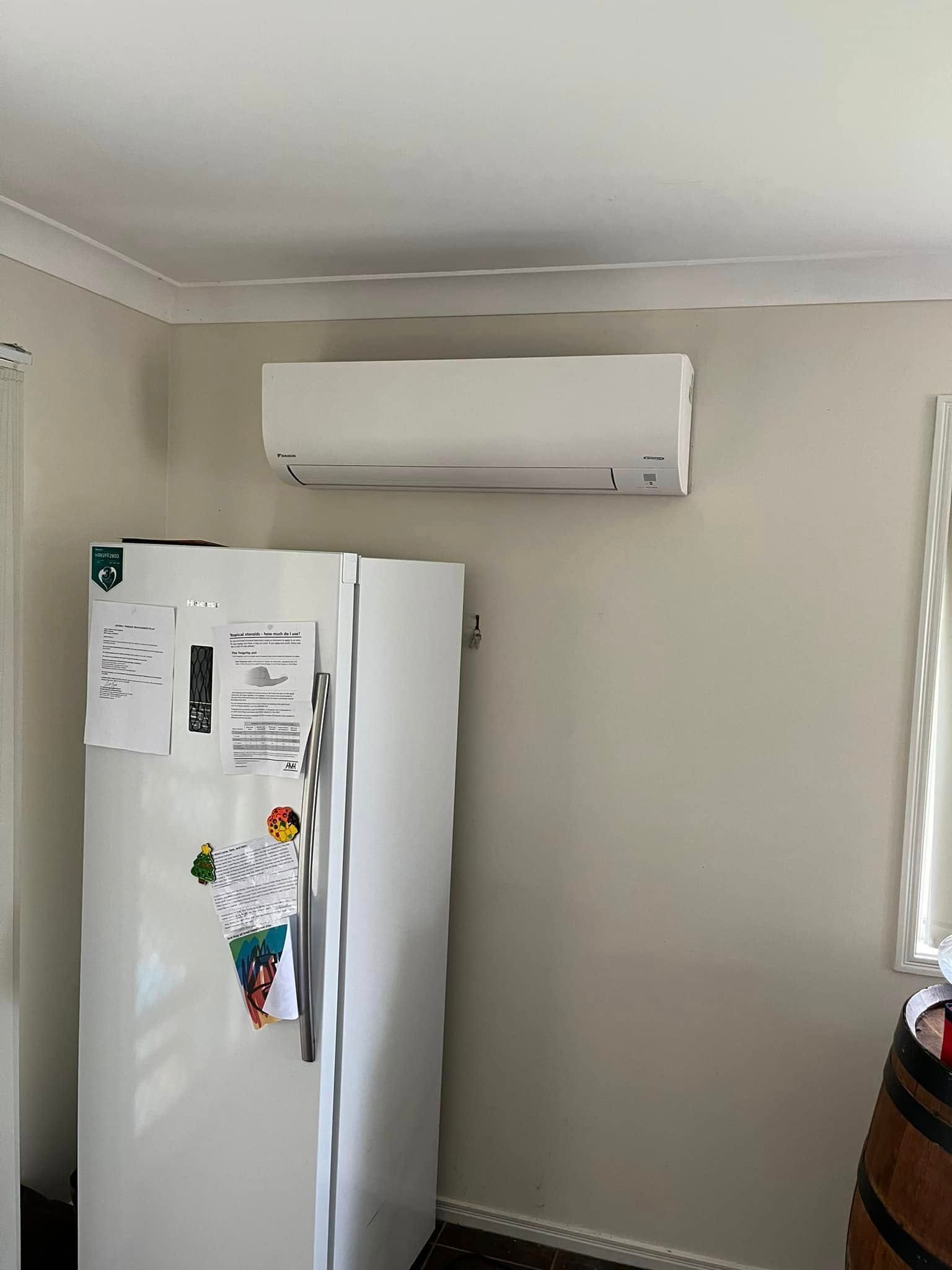 A White Wall-mounted Air Conditioner Positioned Above a White Refrigerator — OHMY Electrical Contractors in Carina, QLD
