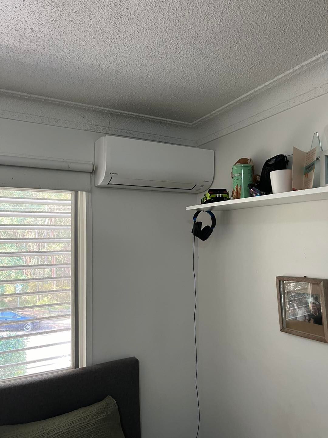 A Wall-mounted White Air Conditioner is Positioned Above a Window and a Shelf — OHMY Electrical Contractors in Carina, QLD