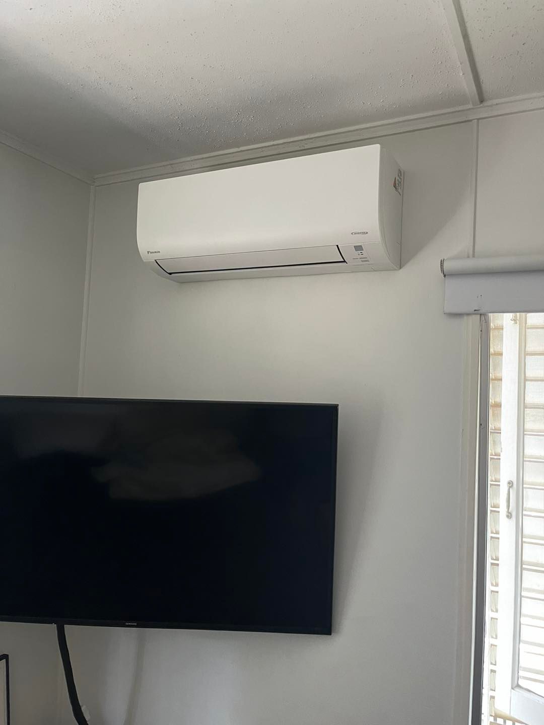 A Wall-mounted White AC Unit Installed Above a Television in a Room — OHMY Electrical Contractors in Bulimba, QLD