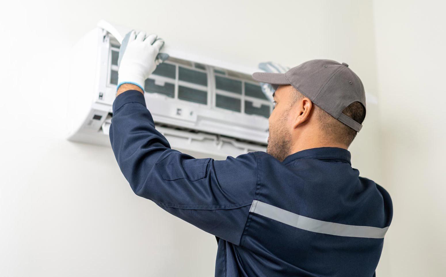 A Technician in a Blue Uniform and Cap Installing a White Wall-mounted AC — OHMY Electrical Contractors in Coorparoo, QLD