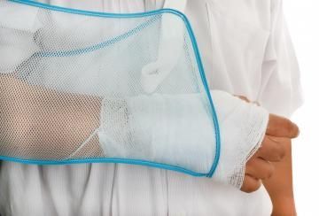 A person wearing a white shirt has their arm supported in a blue-trimmed white mesh medical sling.
