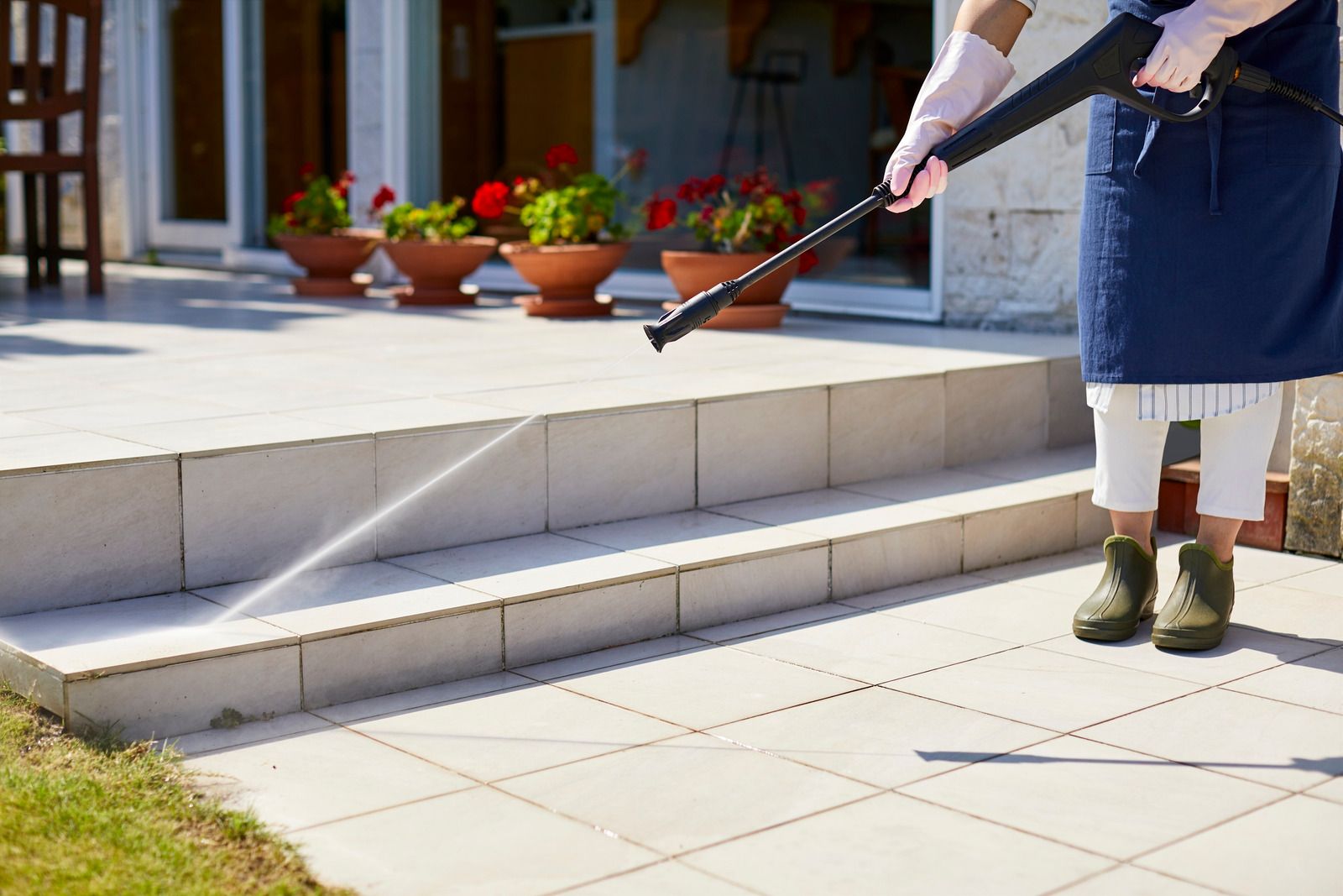 Person pressure-washing stone steps outside a building near potted flowers
