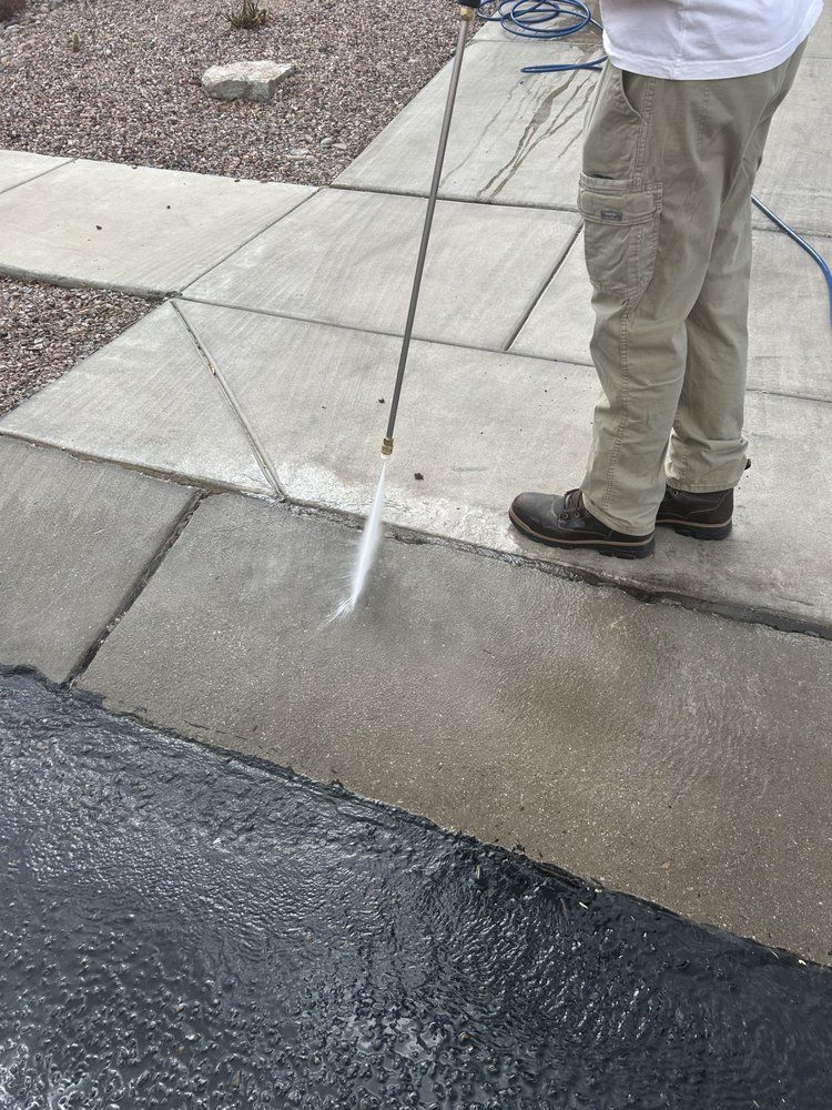 A person is cleaning a sidewalk with a high pressure washer.