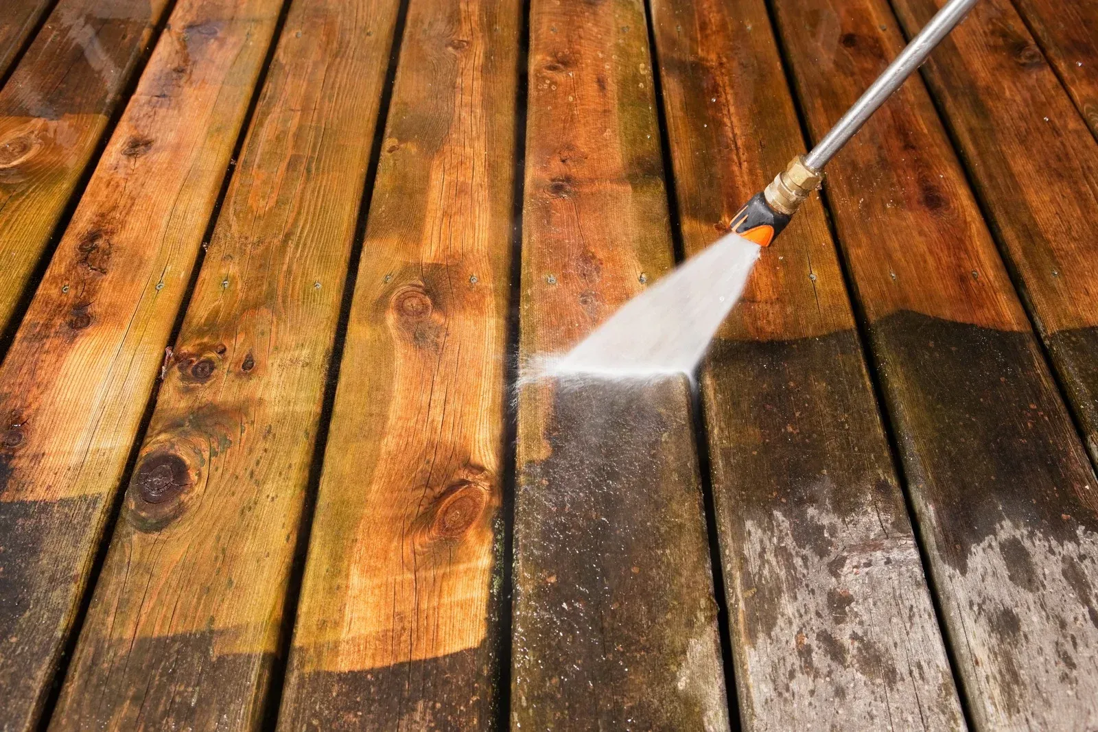 A man is cleaning a fence with a high pressure washer.