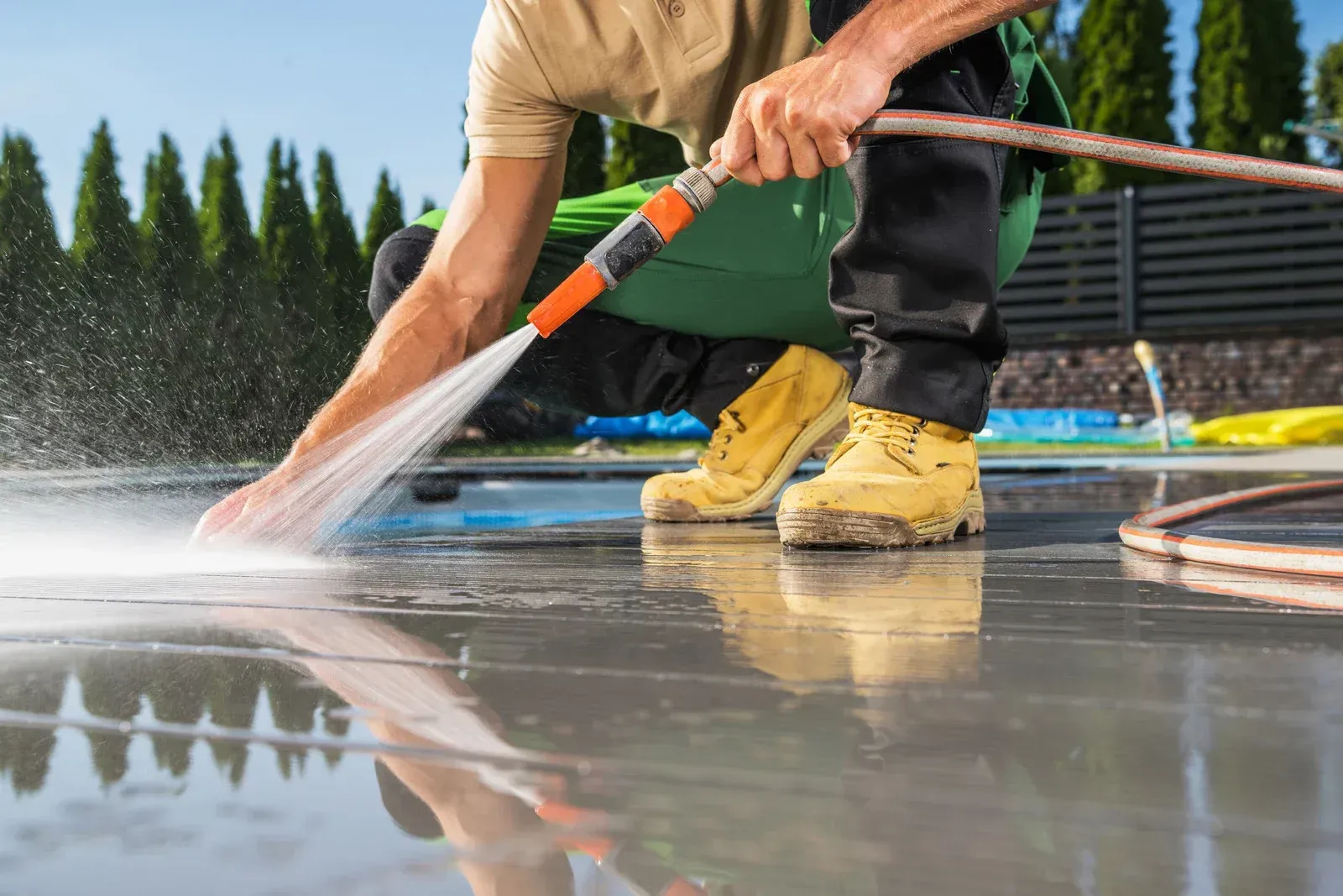 A person is cleaning a wooden fence with a high pressure washer.