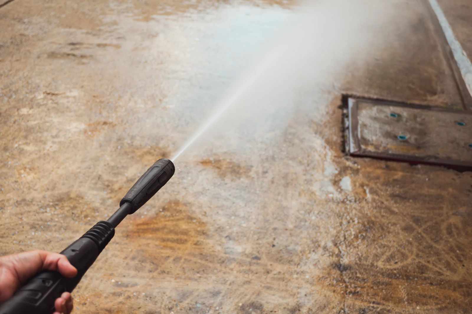 A person pressure-washing a concrete surface, removing dirt.