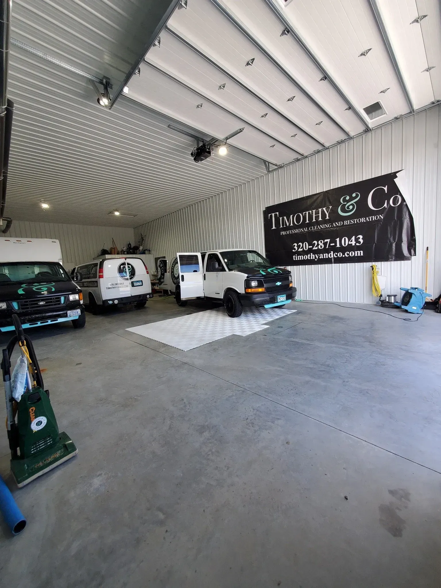 A white van is parked in a garage with a large black banner hanging from the ceiling.