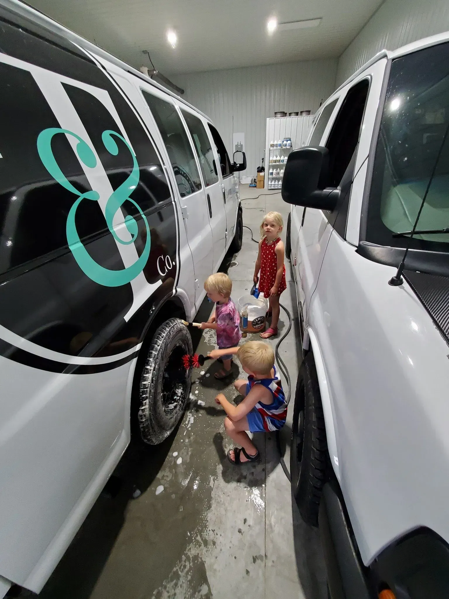 A group of children are standing next to a row of white vans in a garage.