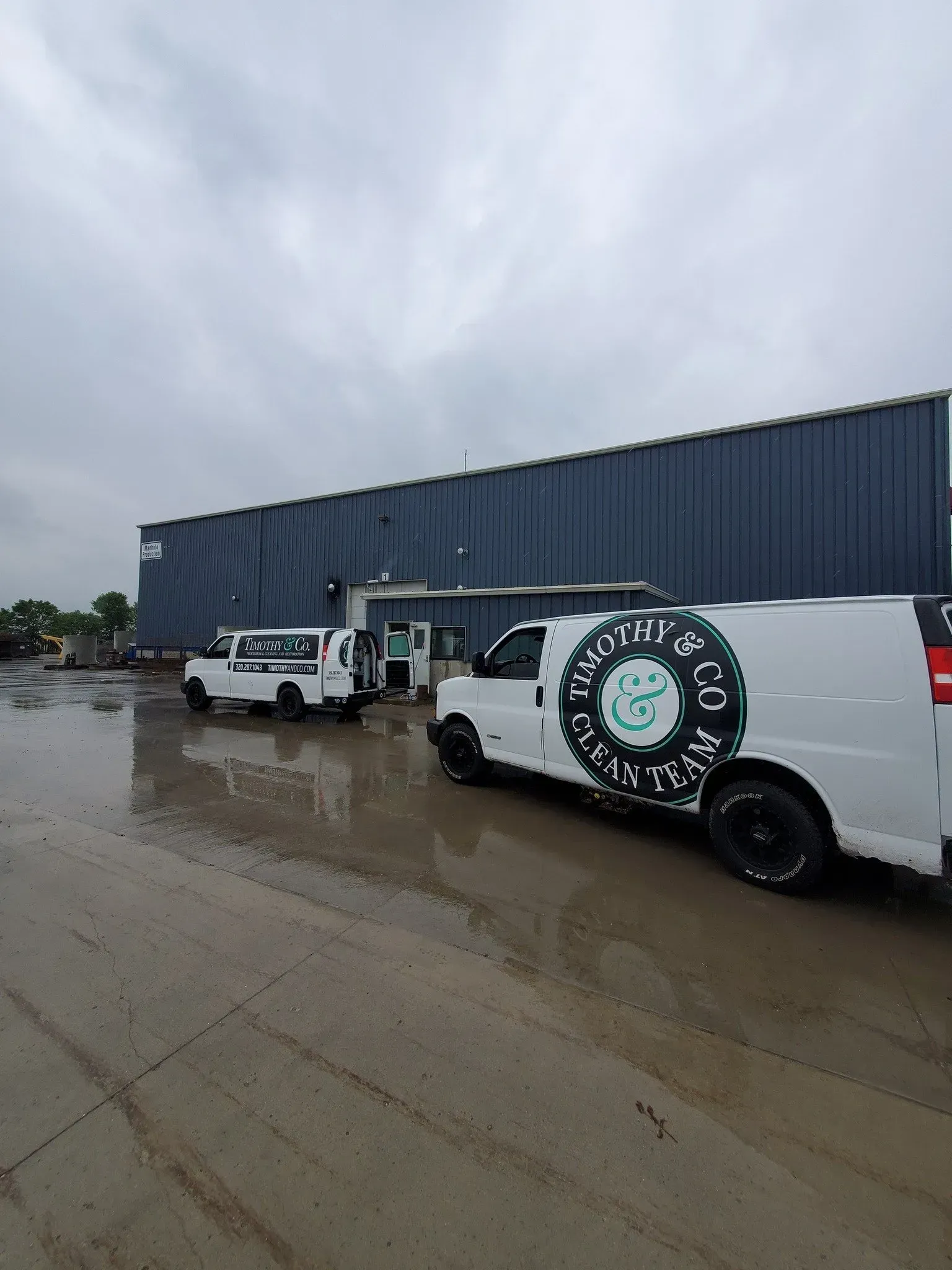 Three white vans are parked in front of a building on a rainy day.