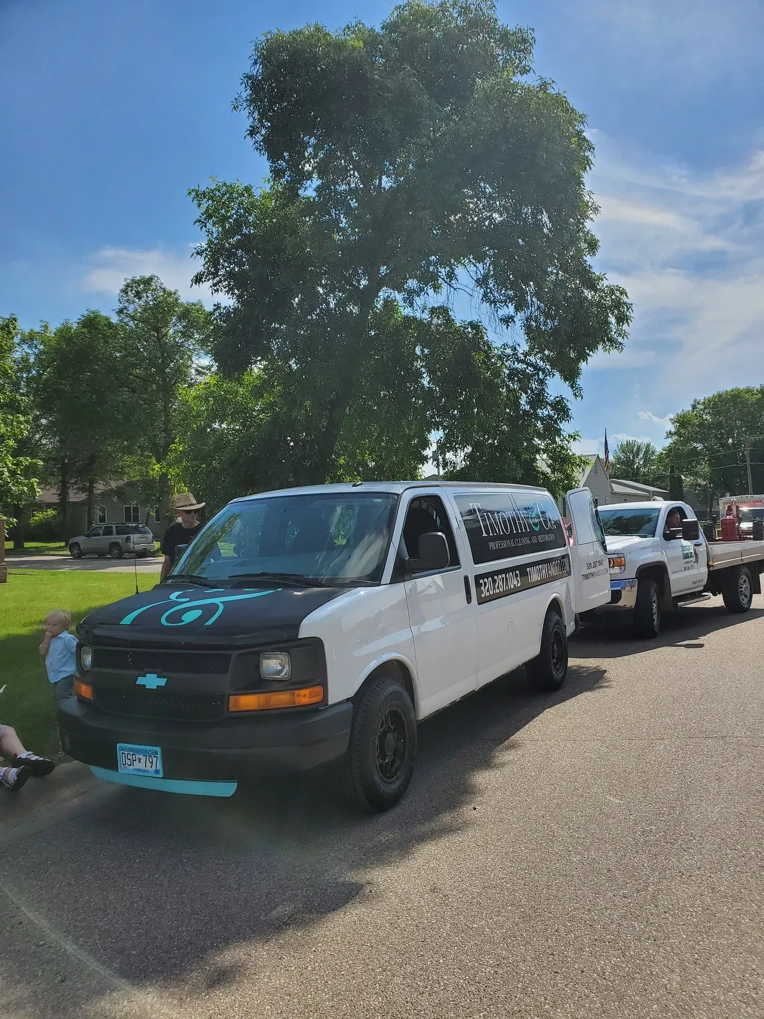 A white van is parked on the side of the road next to a tree.