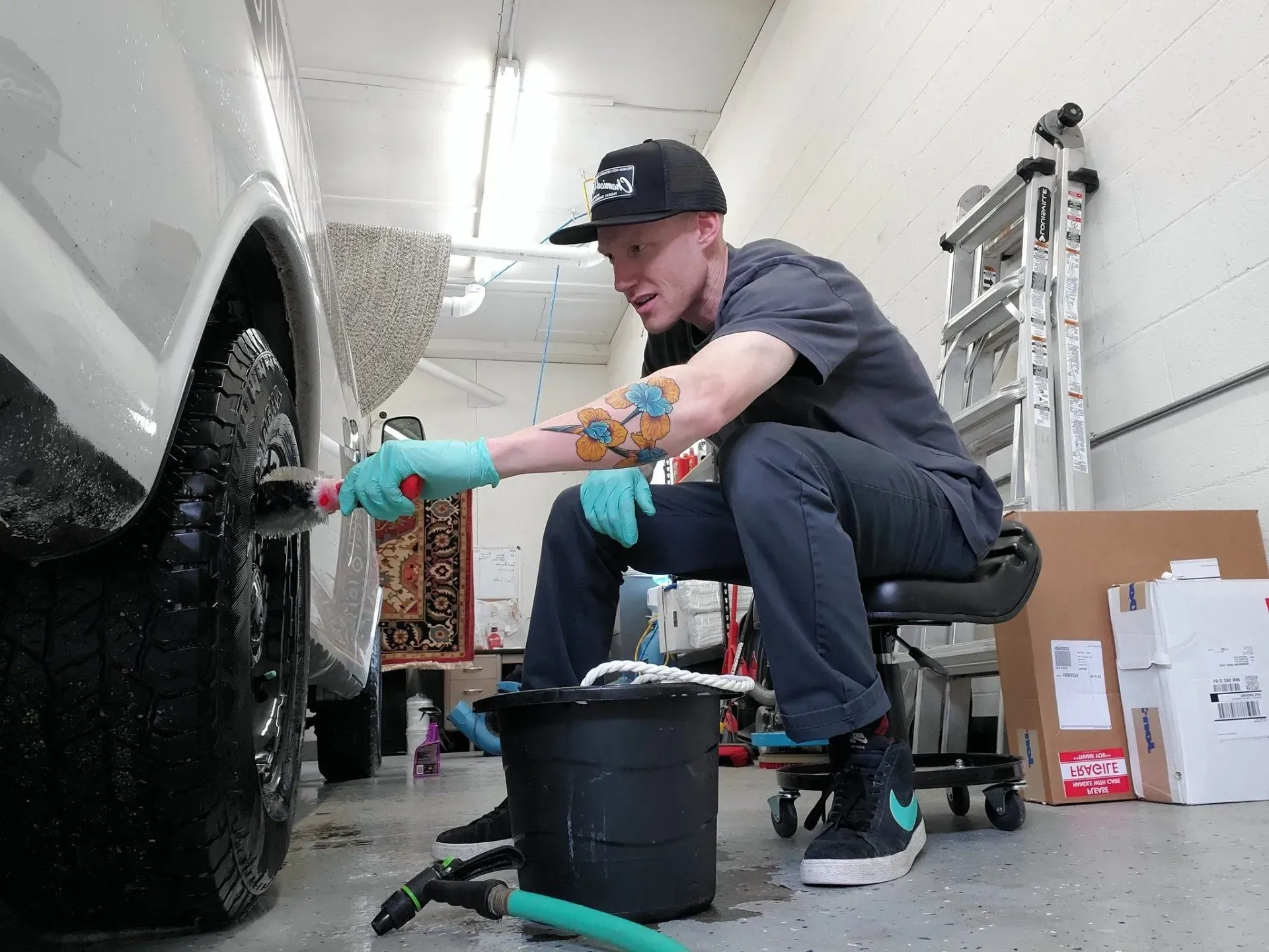 A man is sitting on a stool cleaning a car with a hose.