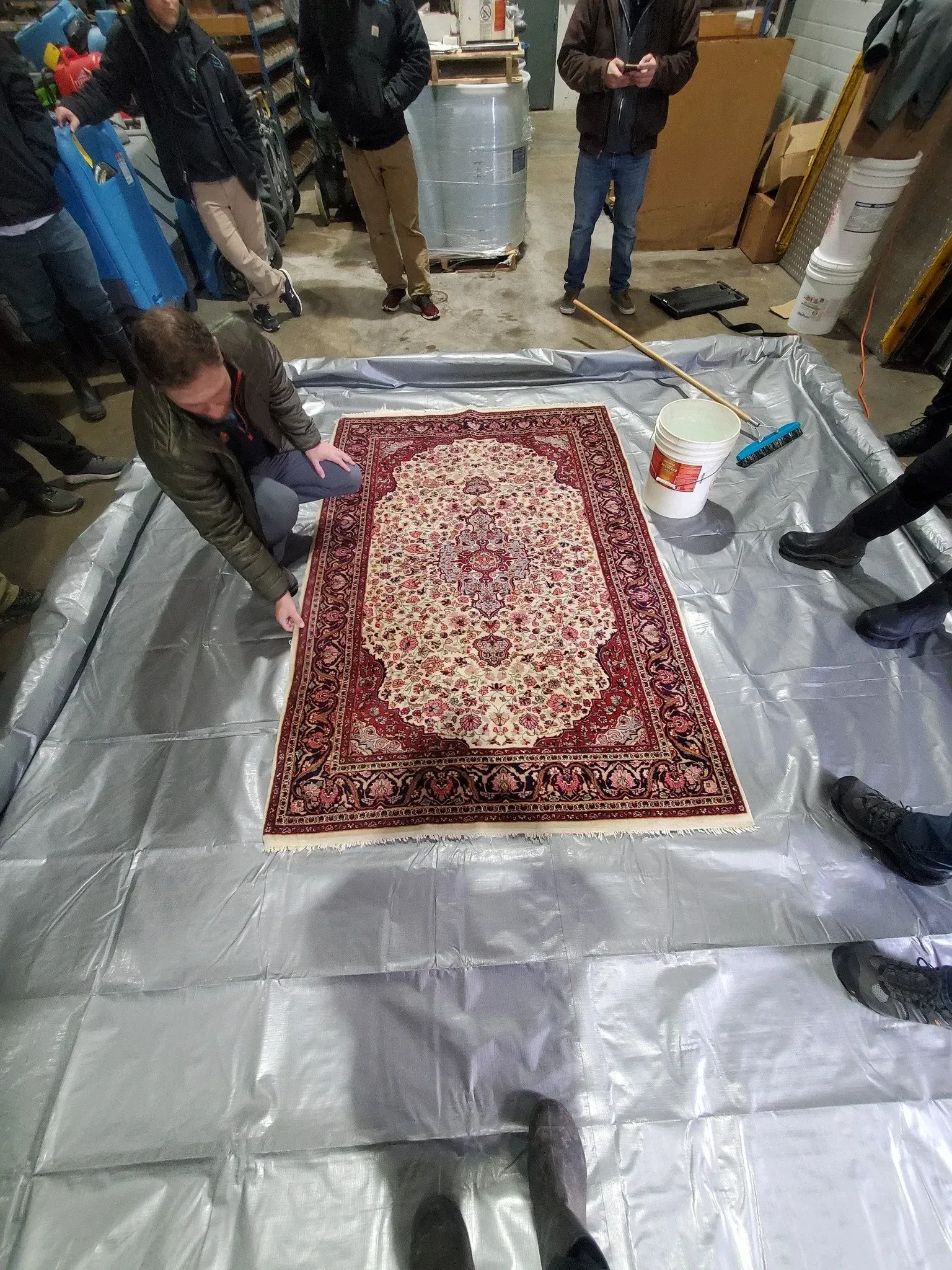 A group of people are sitting around a rug on a tarp.