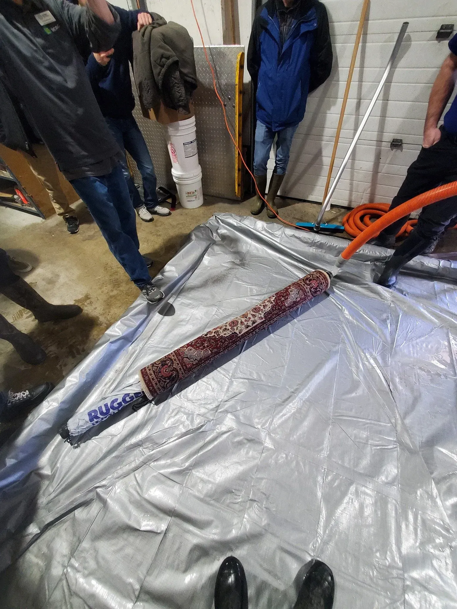 A group of people are standing around a tarp in a garage.