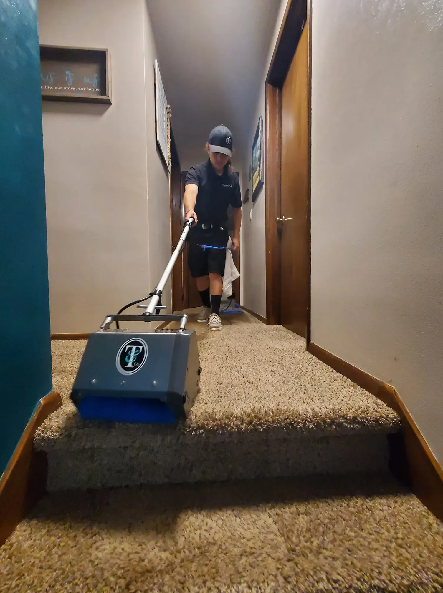A woman is cleaning a carpet with a machine in a hallway.