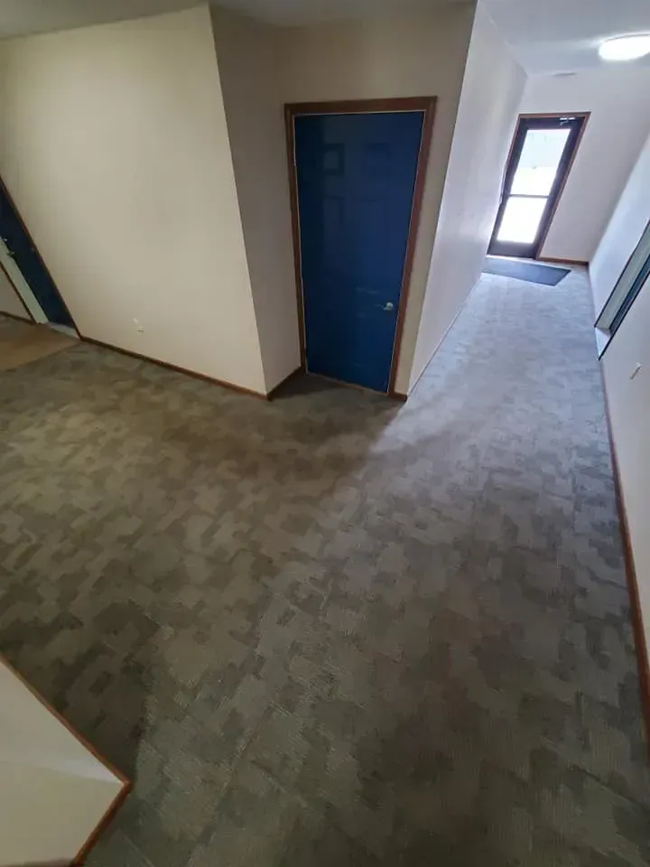 A hallway with a blue door and a carpeted floor.