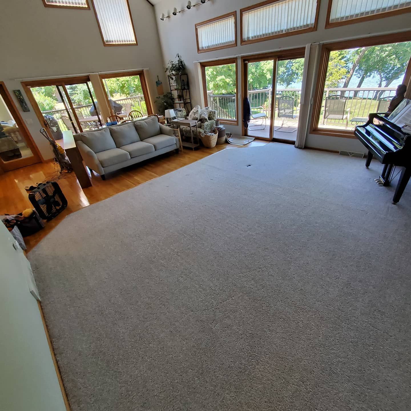 A living room with a couch , piano , and lots of windows.